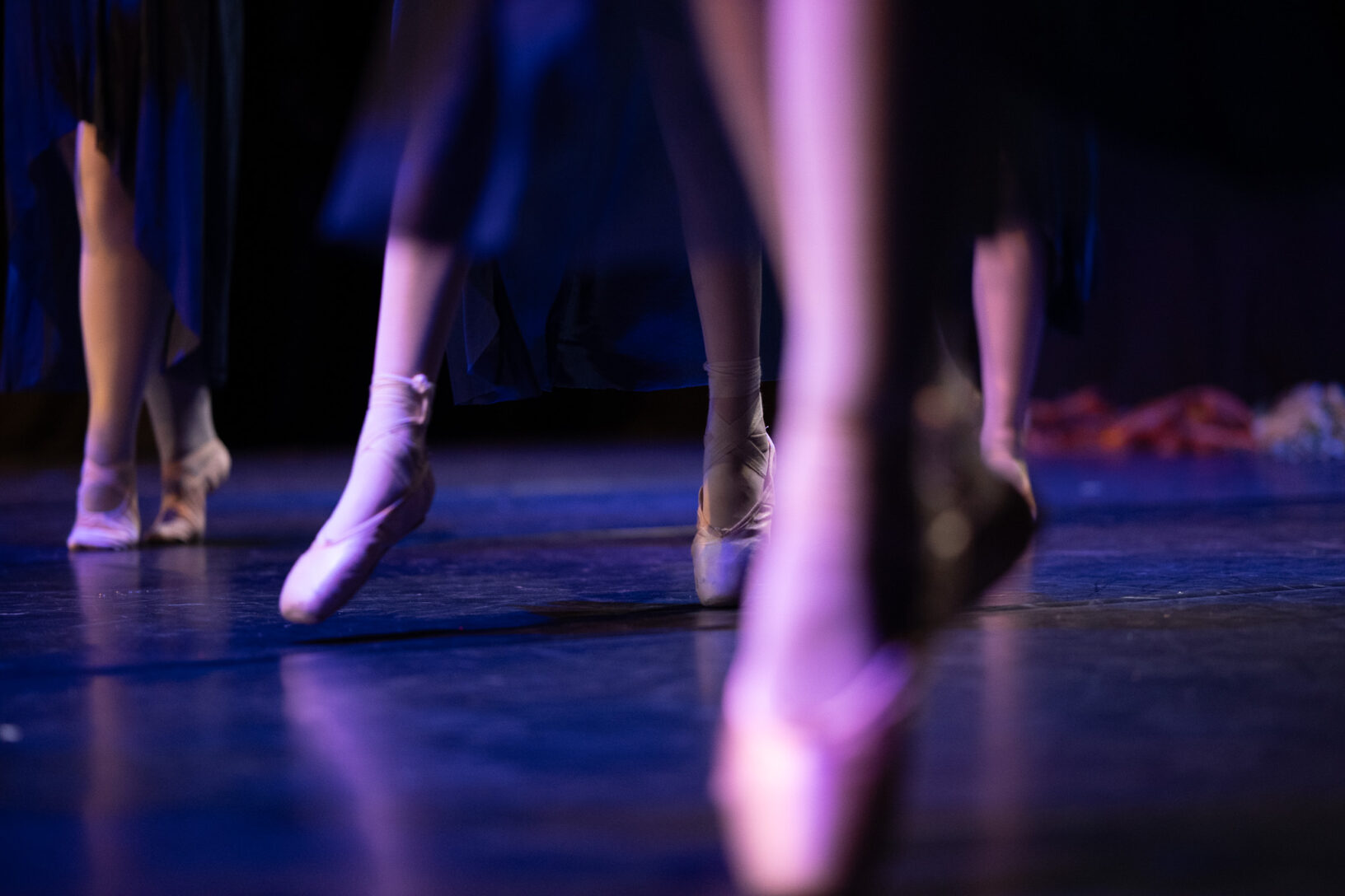 Irene K. - Close-up of Ballett dancers' feet on stage in pink pointe shoes and dark, flowing costumes, with soft lighting highlighting the elegance and movement of their Tanzkurse.