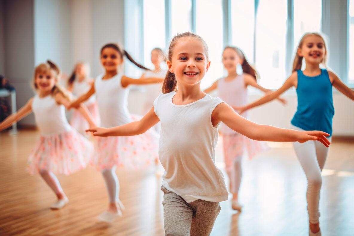Irene K. - Eine Gruppe junger Mädchen in Tanzkleidung übt in einem hellen Studio Ballett und Modern Jazz. Sie lächeln und strecken ihre Arme aus, während sie sich im Einklang bewegen. Das Sonnenlicht fällt durch große Fenster im Hintergrund - ein inspirierender Tanzkurs-Moment.