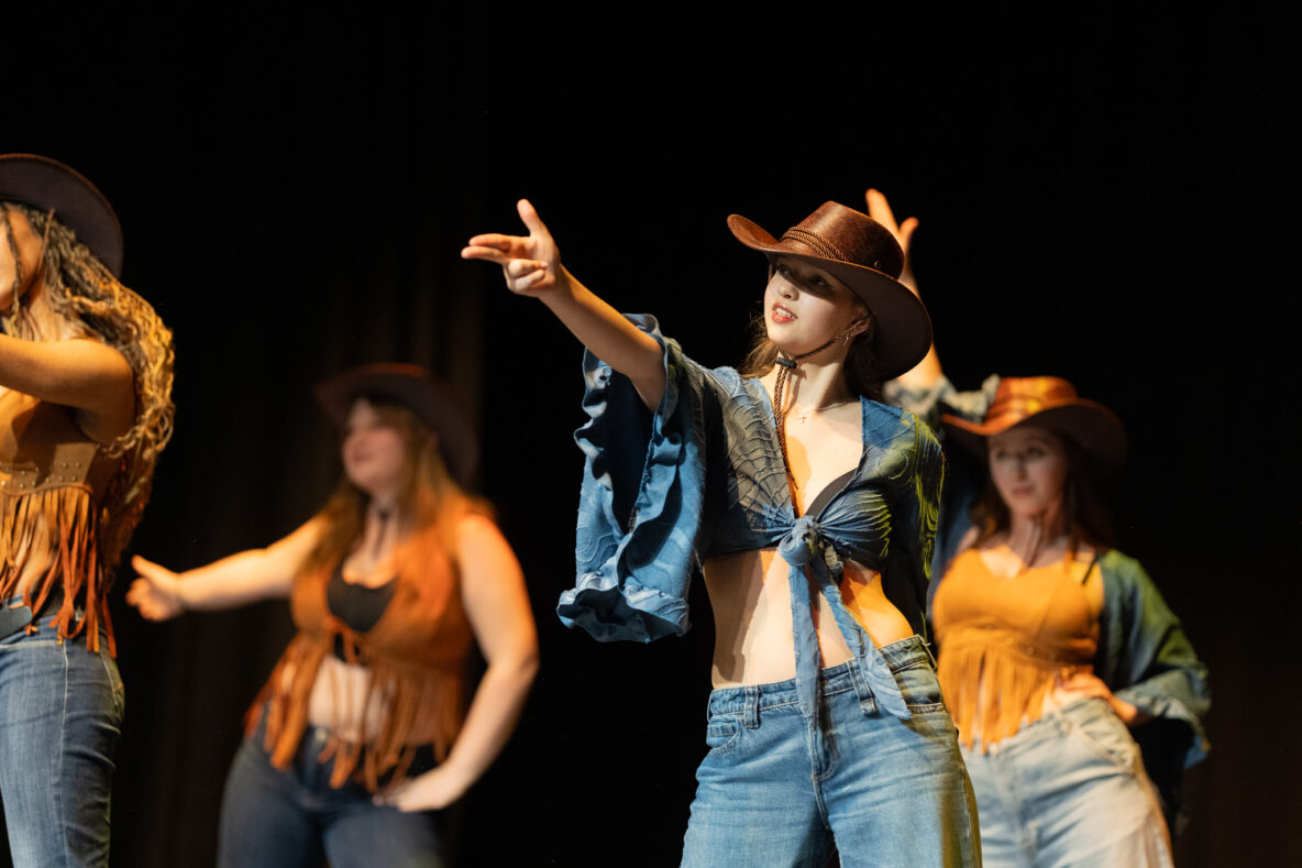 Irene K. - Vier Frauen mit Cowboyhüten, Jeans und Fransenoberteilen führen auf der Bühne in Eupen einen choreografierten Modern-Jazz-Tanz auf, wobei eine Frau im Vordergrund dramatisch mit dem Finger nach außen zeigt.